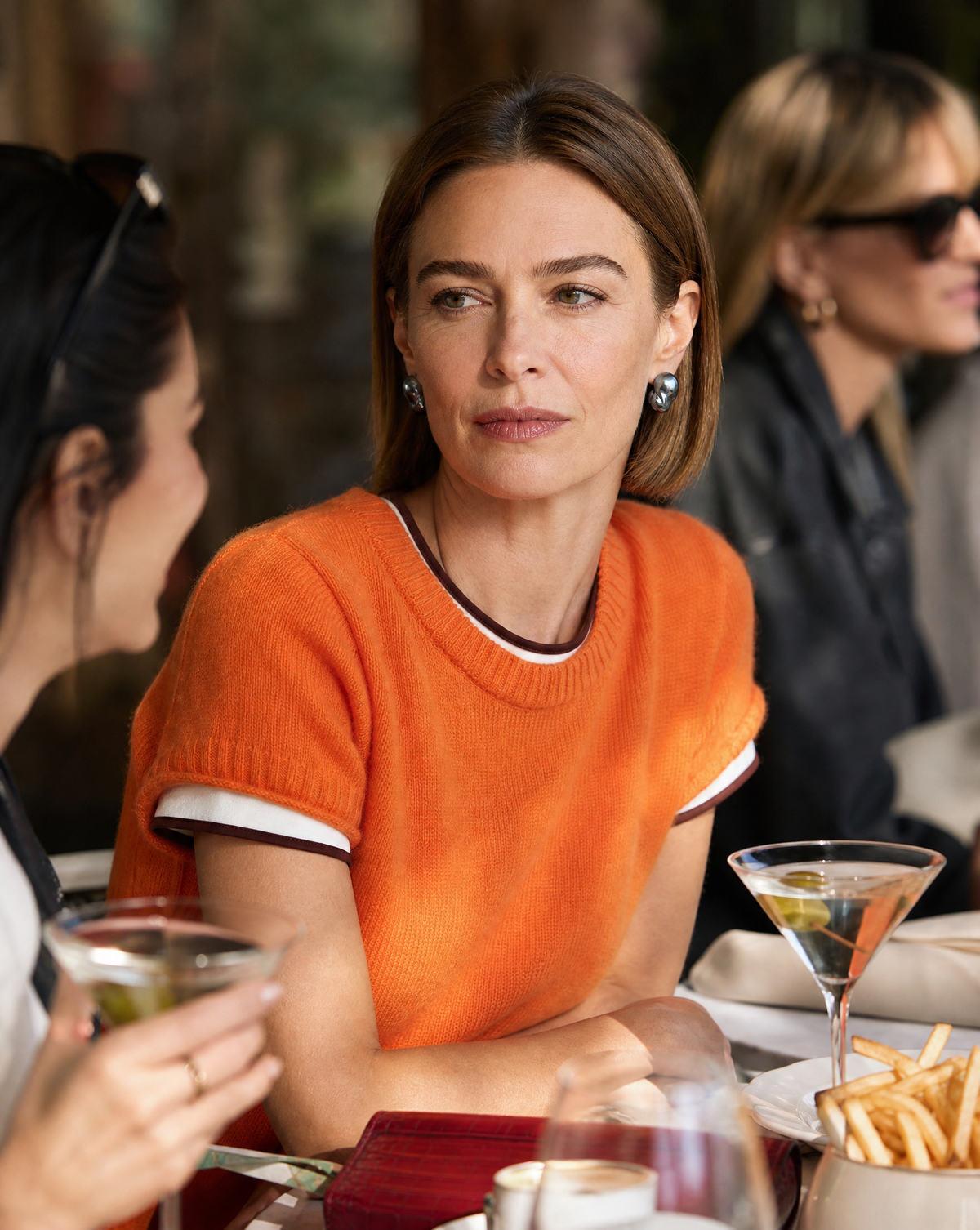 Café table scene with a woman in an orange sweater wearing Perle Noire peacock baroque pearl earrings