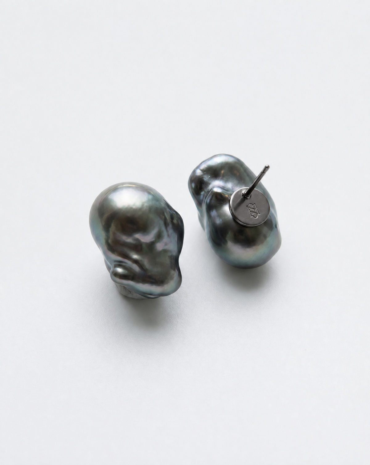 Perle Noire peacock baroque pearl earrings, one turned to show its monogrammed black rhodium plated back