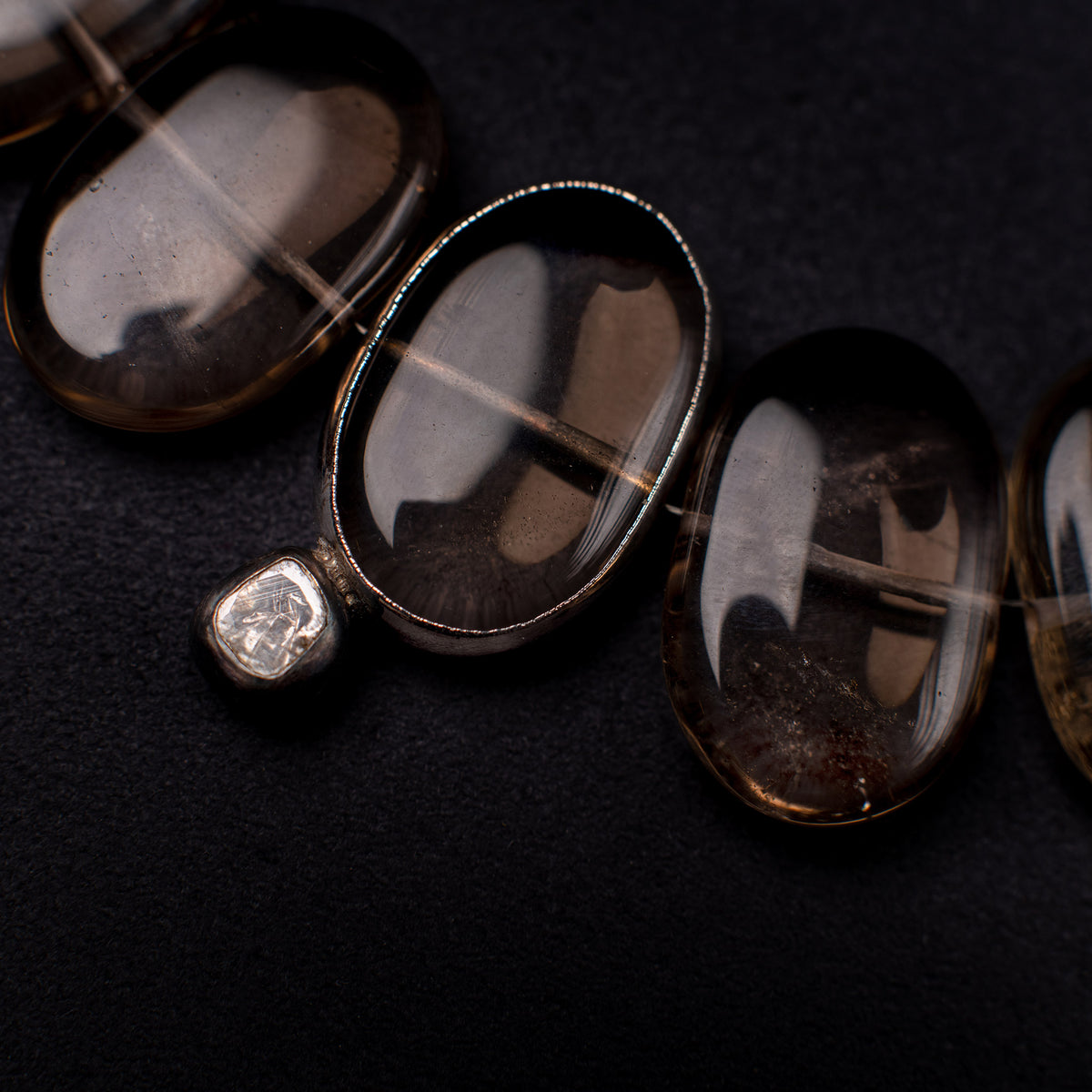 Close-up of Flux smoky quartz ovals, one silver-tone rimmed, with a diamond accent on black