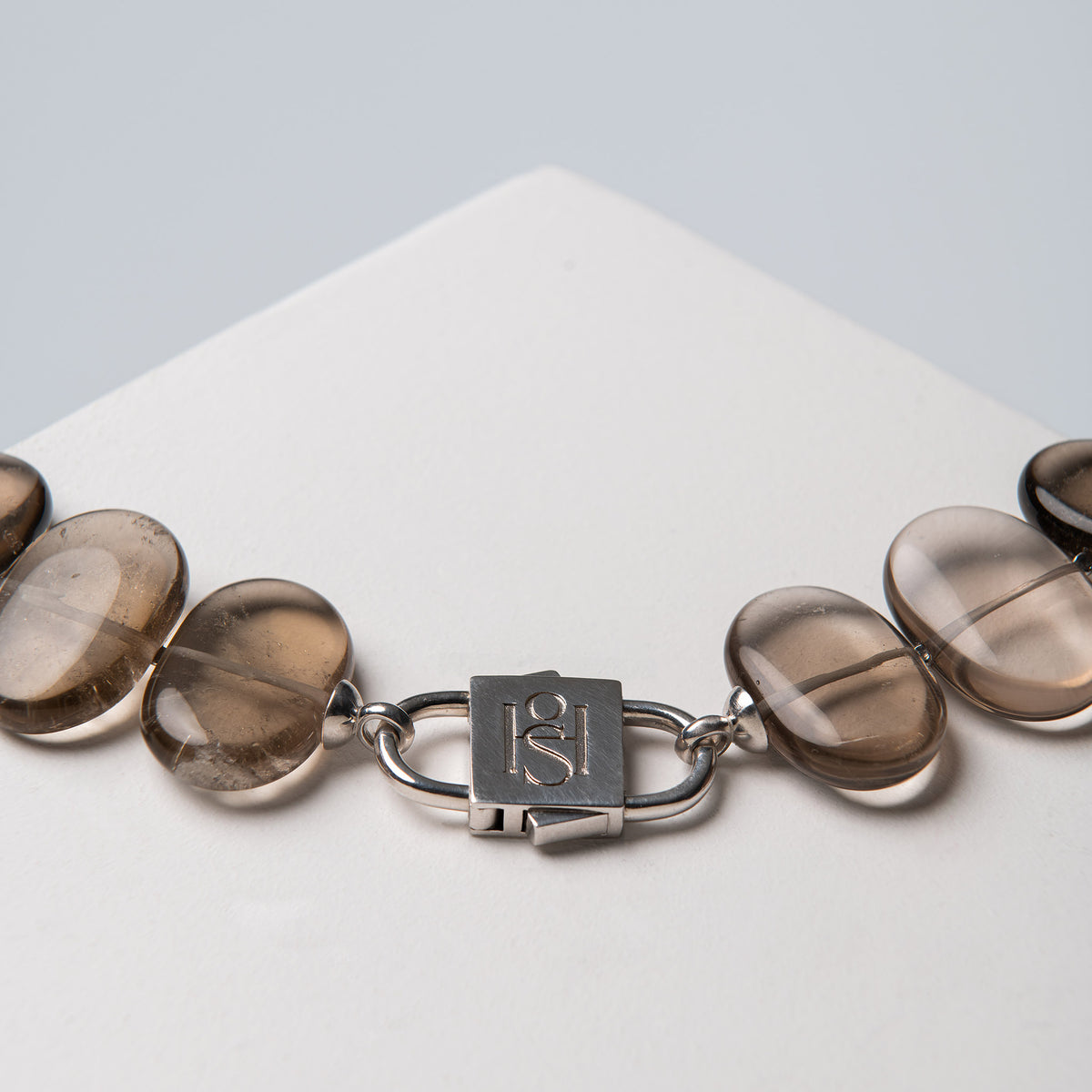Silver-tone HoS Lock joining Flux smoky quartz ovals, close-up on a white block
