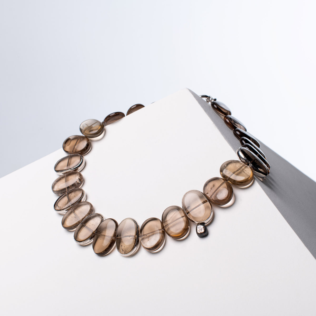 Flux smoky quartz necklace with silver-tone rims on some stones and a diamond accent, on a white block