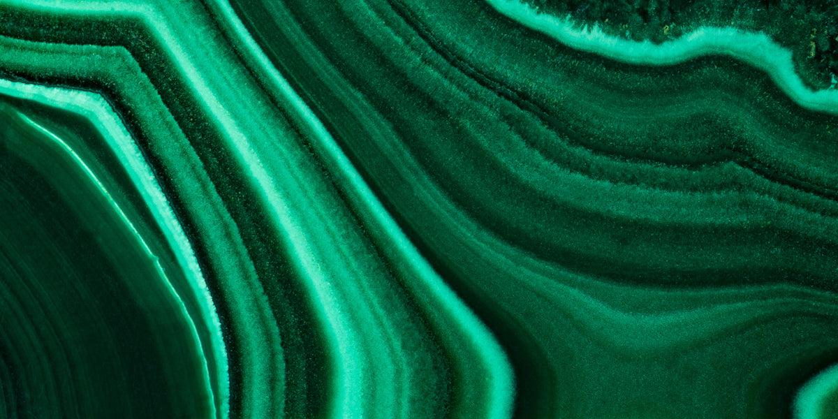 Wide close-up of green malachite with sweeping light and dark bands, a material reference for the Anohni necklace