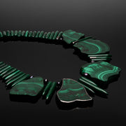 Close view of Anohni malachite stones, spike beads and black pearls on a black reflective surface