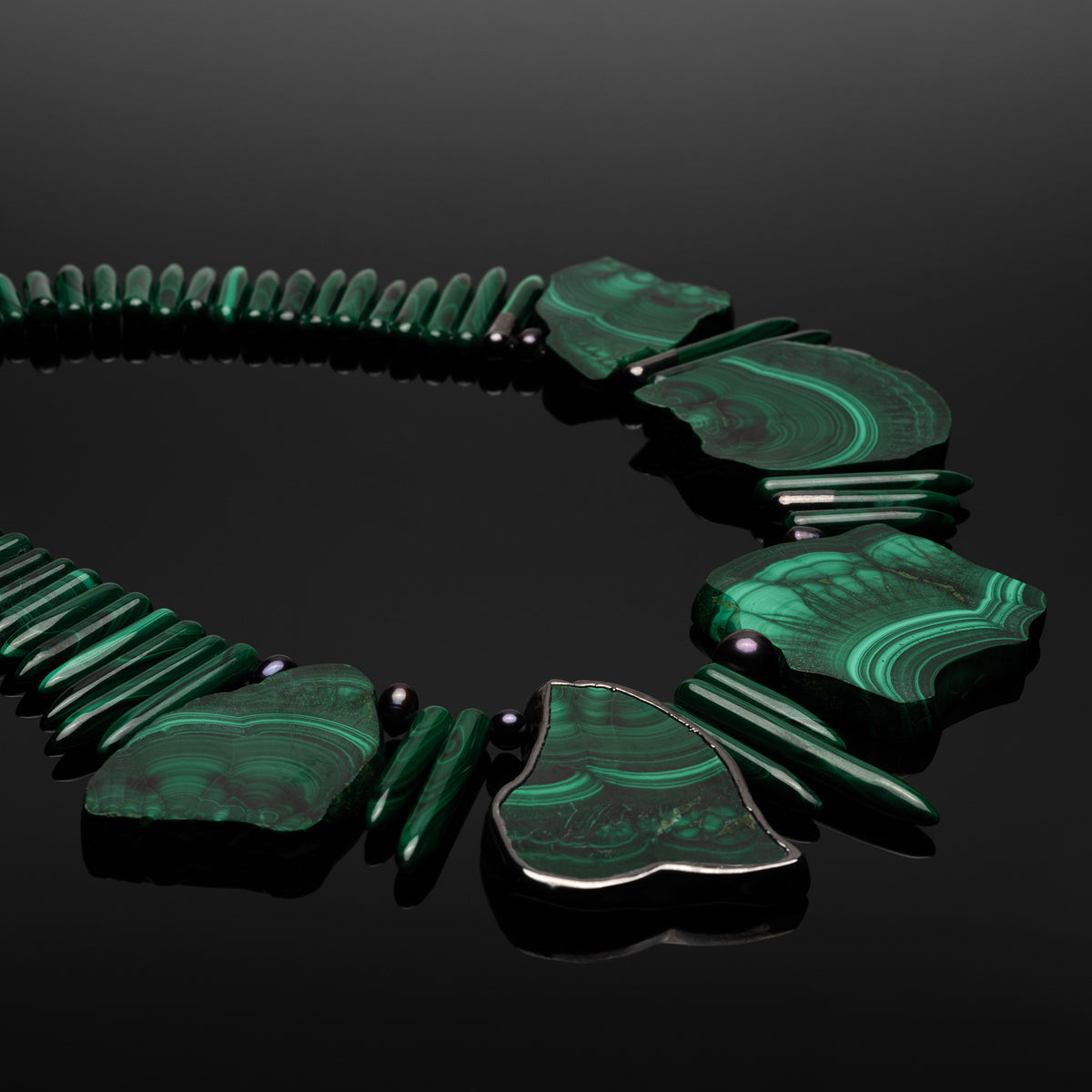 Close view of Anohni malachite stones, spike beads and black pearls on a black reflective surface