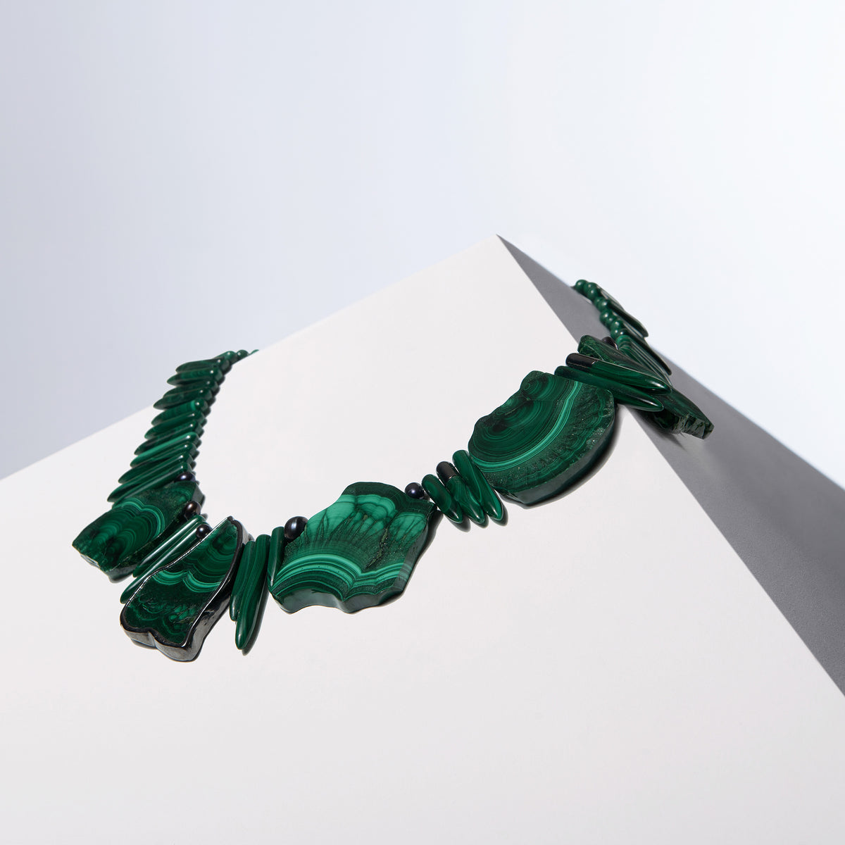Anohni malachite necklace with large cut stones, spike beads and small black pearls on a white block