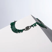 Back of the Anohni malachite necklace with a dark HoS Lock between spike beads, on a white block