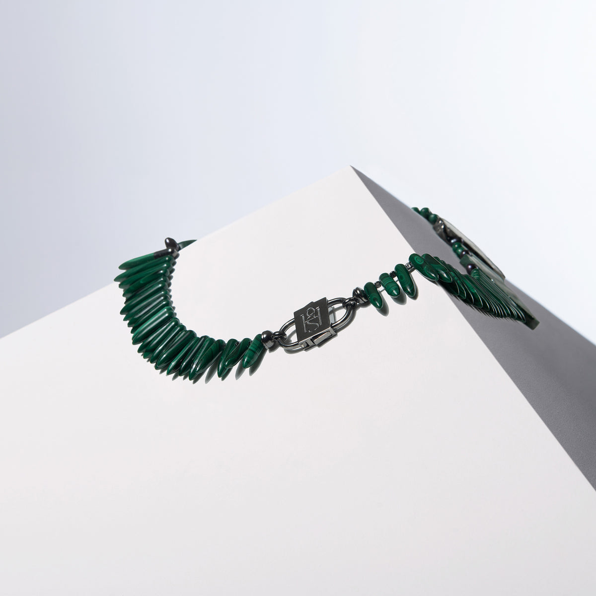 Back of the Anohni malachite necklace with a dark HoS Lock between spike beads, on a white block