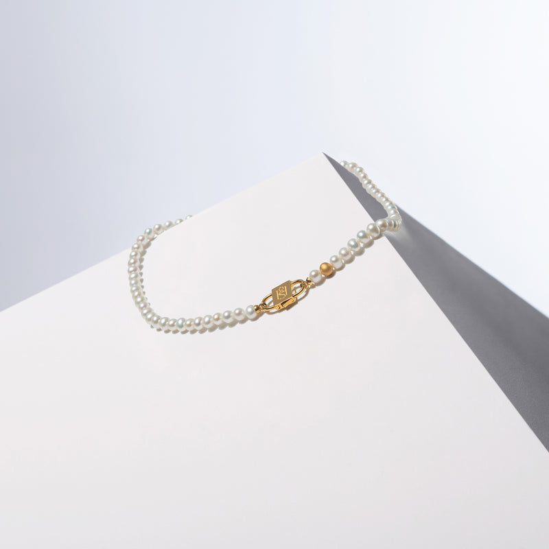 Auriluna oval pearl necklace with a sandblasted gold-tone bead and gold-tone HoS Lock on a white block
