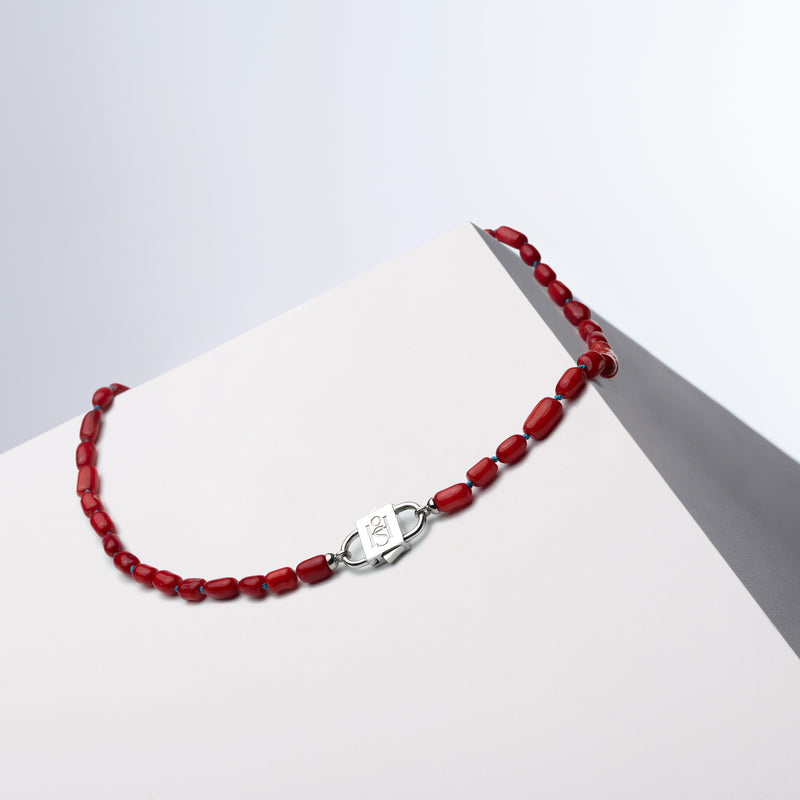 Bebe Rouge silk-knotted coral necklace with HoS Lock draped over a white block