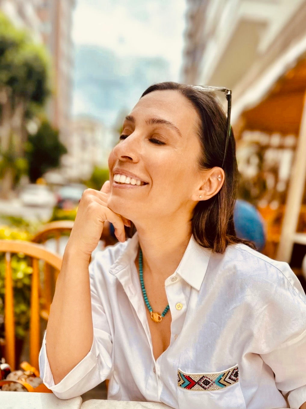 Smiling woman at a café terrace wearing Bebe Turquoise necklace with HoS Lock and a white shirt