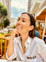 Smiling woman at a café terrace wearing Bebe Turquoise necklace with HoS Lock and a white shirt