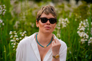 Bebe Turquoise necklace with HoS Lock worn with a white shirt and sunglasses among white flowers