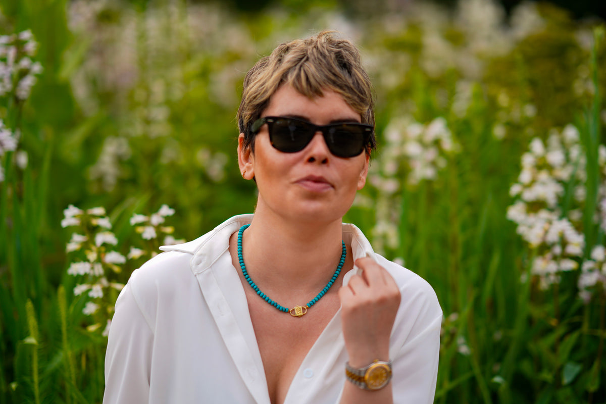 Bebe Turquoise necklace with HoS Lock worn with a white shirt and sunglasses among white flowers
