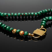 Iris malachite necklace detail with gold-tone HoS Lock and gold-filled ornaments on a black surface