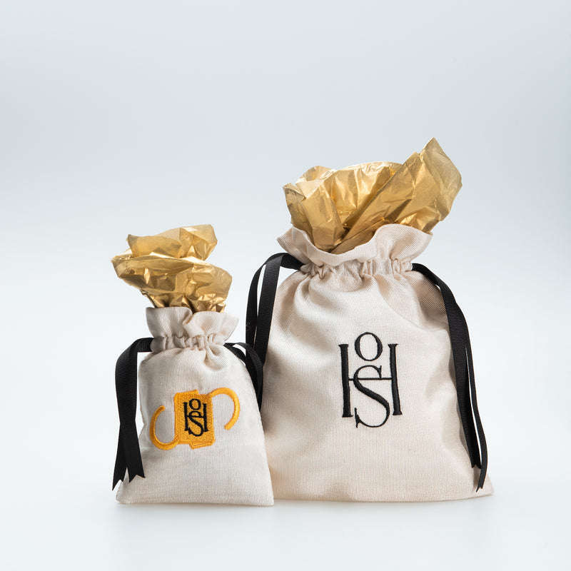 Two drawstring jewelry pouches with embroidered HoS monograms, black ribbons and gold tissue