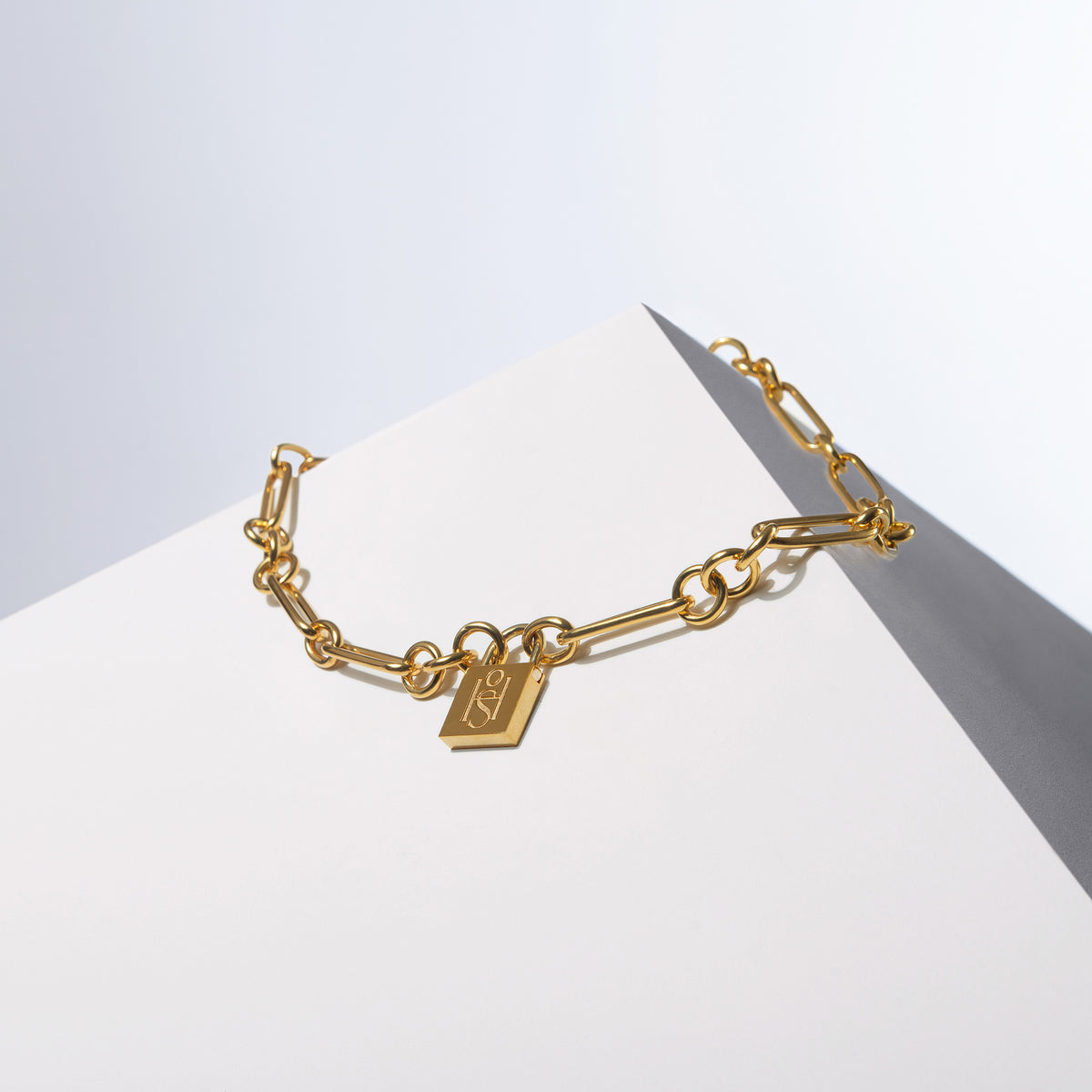Medium Trombone Chain Necklace with HoS Padlock hanging from the links, on a white block