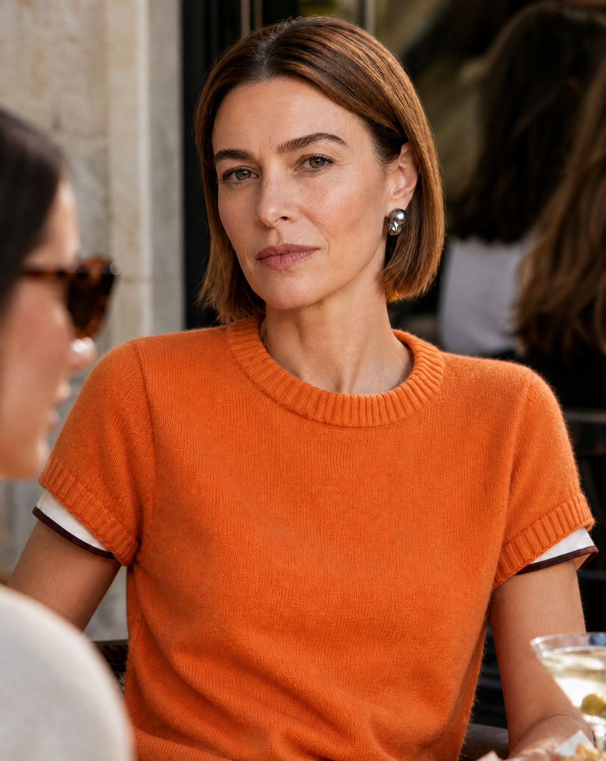 Woman in an orange sweater facing the camera at a café, wearing a Perle Noire baroque pearl earring