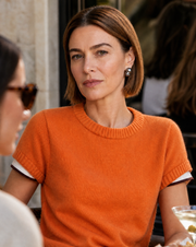Woman in an orange sweater facing the camera at a café, wearing a Perle Noire baroque pearl earring