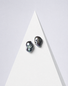 Perle Noire peacock baroque pearl earrings, a pair on a white pyramid against a pale backdrop