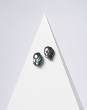 Perle Noire peacock baroque pearl earrings, a pair on a white pyramid against a pale backdrop