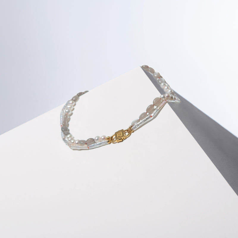 Pikakae Blanc Biwa pearl and pearl-moonstone strands joined by a gold-tone HoS Lock on a white block