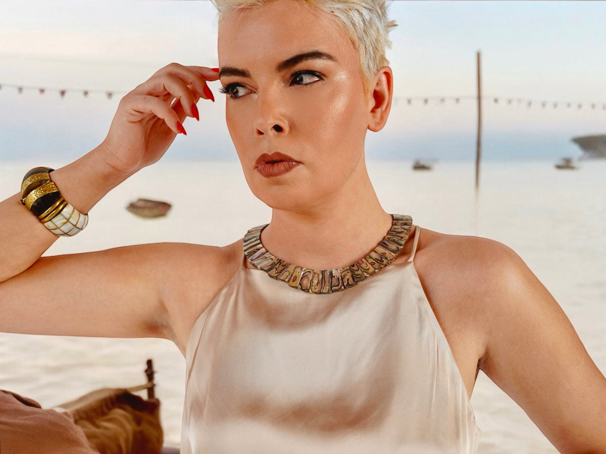 Queen Paua sea shell necklace on a model in a beige satin halter top, beach backdrop