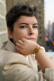Model with chin on hand wearing the Shirin rondelle pearl bracelet with gold-tone HoS Lock, city backdrop