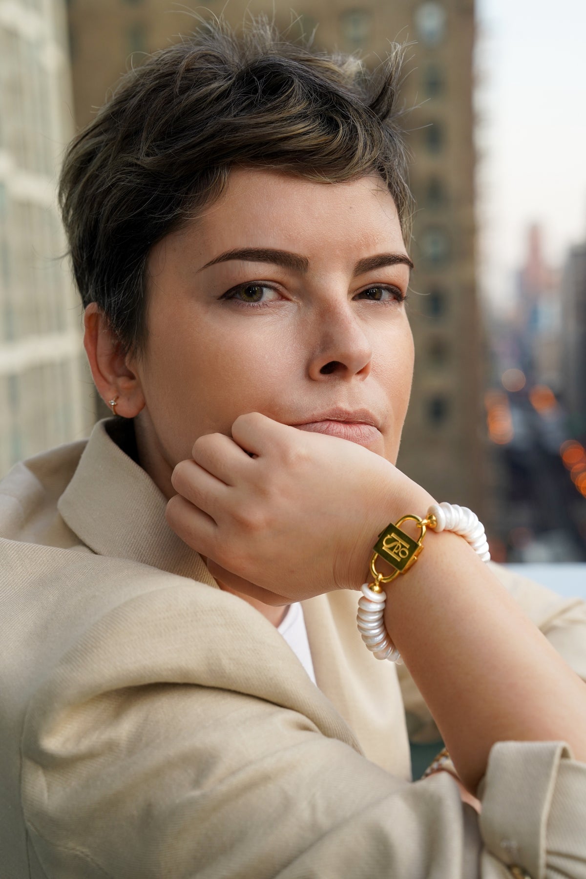 Model with chin on hand wearing the Shirin rondelle pearl bracelet with gold-tone HoS Lock, city backdrop