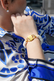 Shirin rondelle pearl bracelet with gold-tone HoS Lock worn with a blue printed shirt, wrist close-up