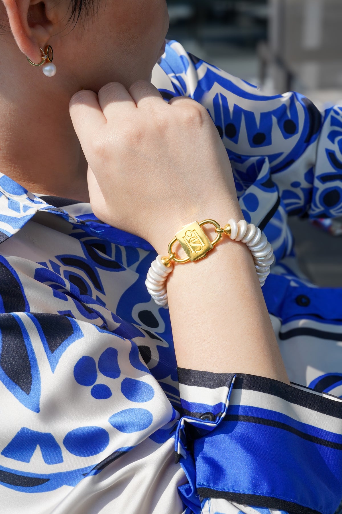 Shirin rondelle pearl bracelet with gold-tone HoS Lock worn with a blue printed shirt, wrist close-up