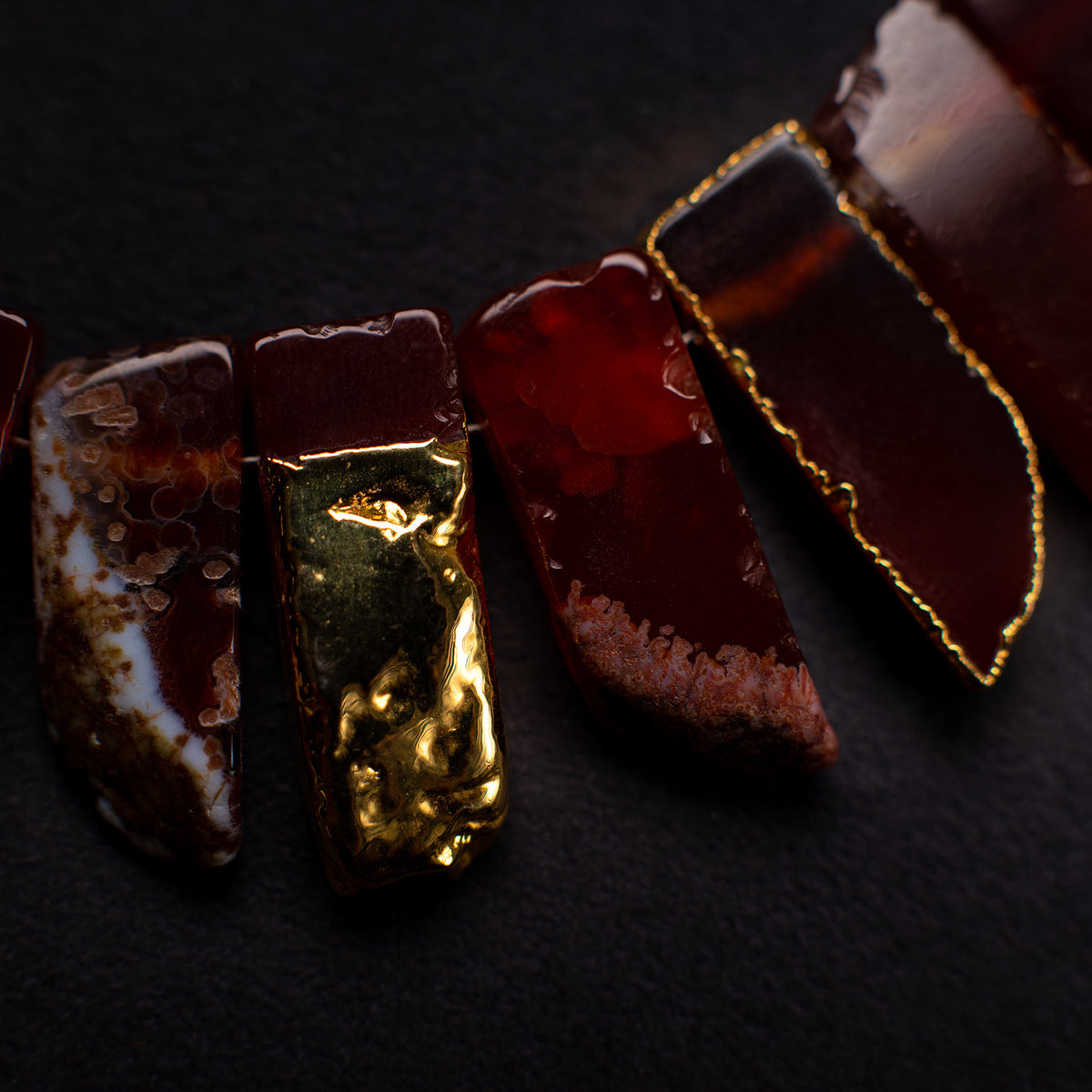 Close-up of Aliye red agate slices, some with gold-tone surface or edging, on a dark background