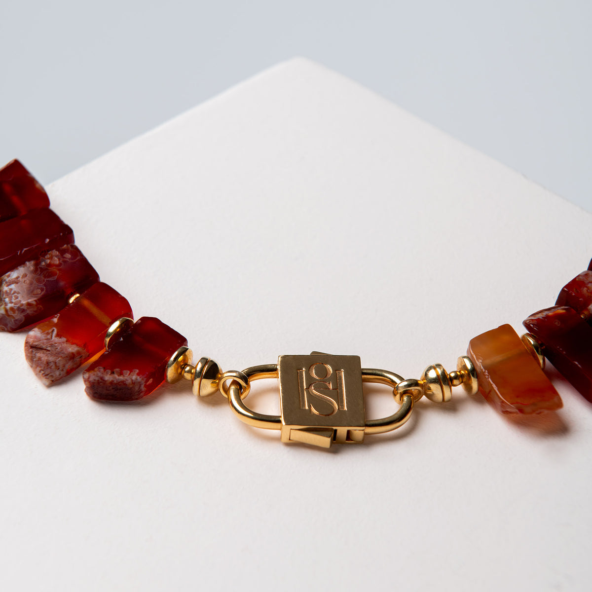 Close-up of the Aliye red agate necklace with gold-tone HoS Lock on a white surface