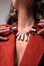 Close-up of the Aliye red agate necklace at the neck, framed by rust-colored jacket lapels