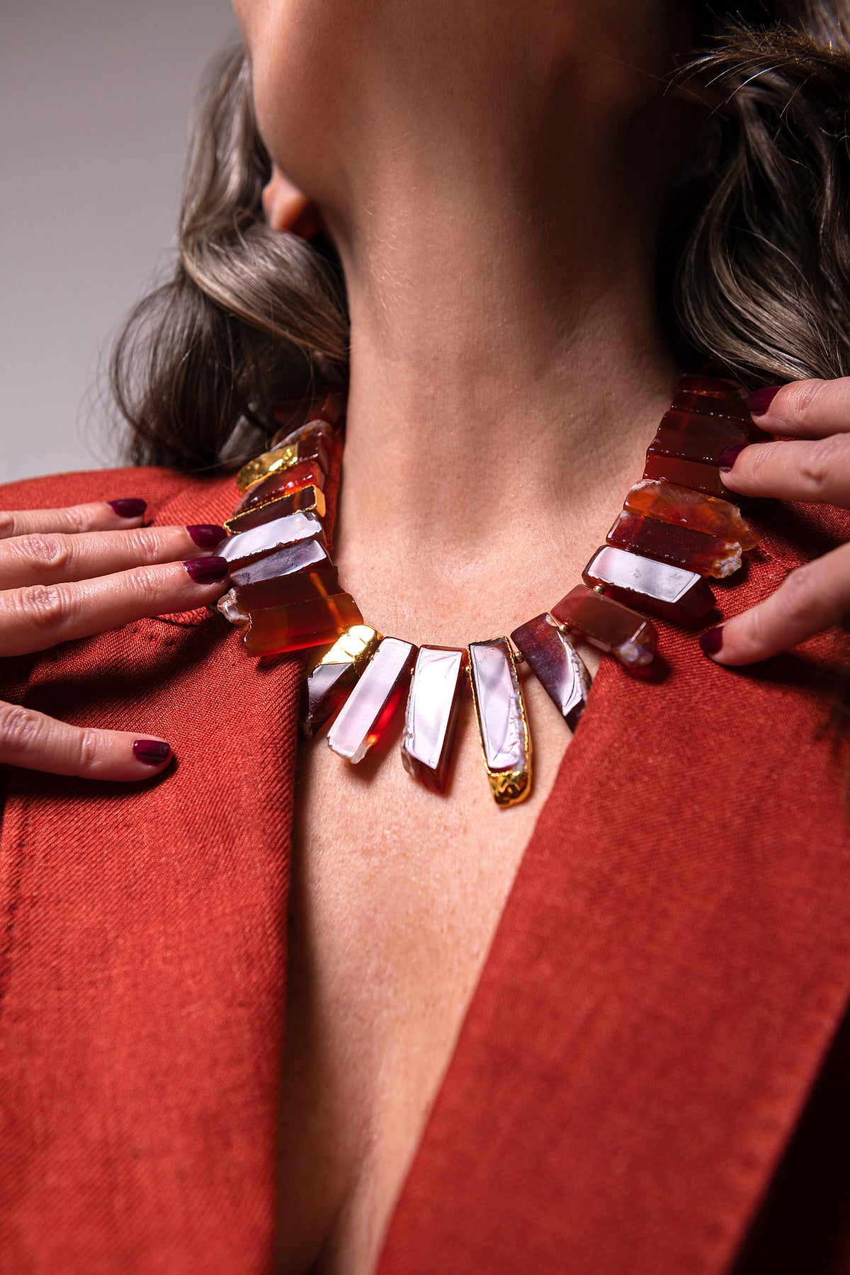Close-up of the Aliye red agate necklace at the neck, framed by rust-colored jacket lapels