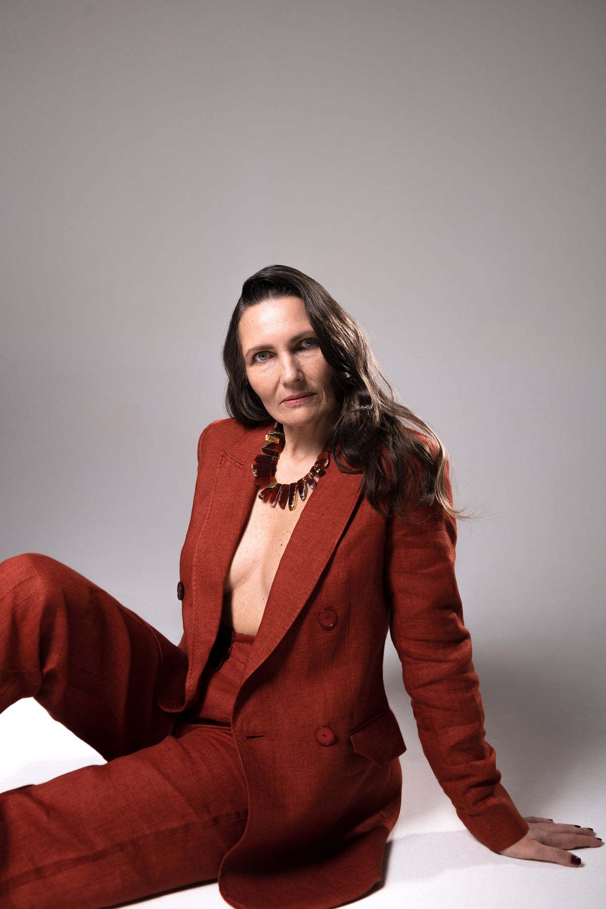 Model in a rust-colored suit seated on the floor wearing the Aliye red agate necklace