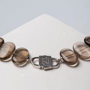 Silver-tone HoS Lock joining Flux smoky quartz ovals, close-up on a white block