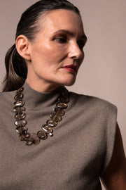 Model in a sleeveless taupe turtleneck wearing Flux smoky quartz necklace, gazing to the side