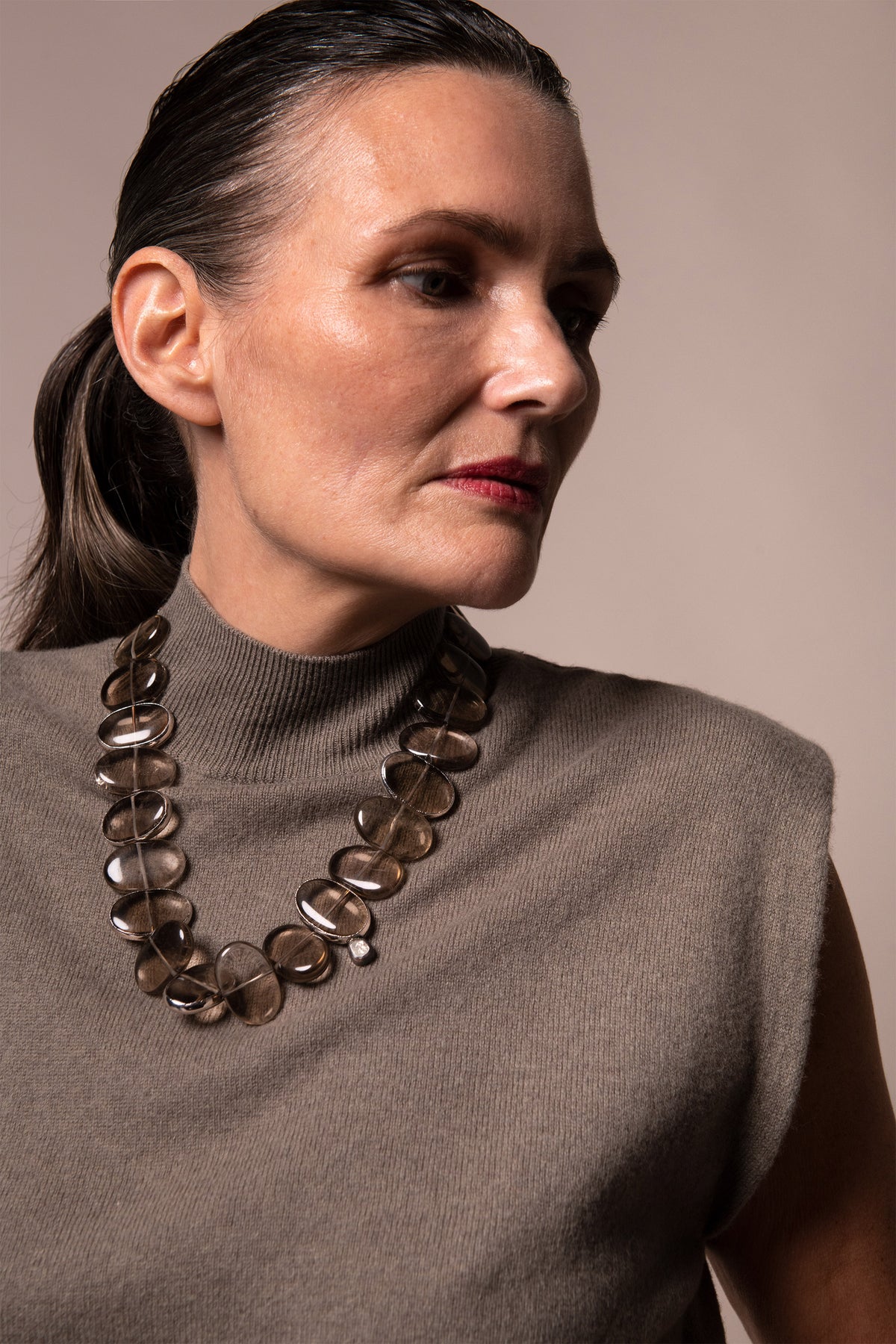 Model in a sleeveless taupe turtleneck wearing Flux smoky quartz necklace, gazing to the side