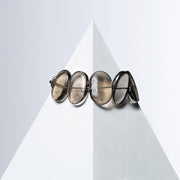 Fluxes bracelet of oval smoky quartz stones, some edged in silver-tone metal, on a white pyramid