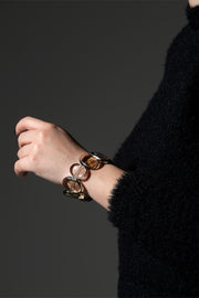 Fluxes smoky quartz bracelet on the wrist showing its oval stones, black knit sleeve on a dark backdrop