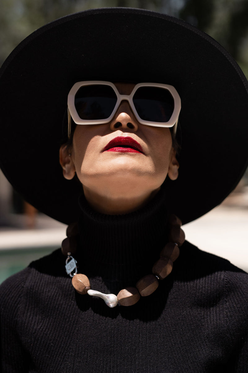 Model in black hat and turtleneck looking up, wearing Light Walden wood and pearl necklace with HoS Lock