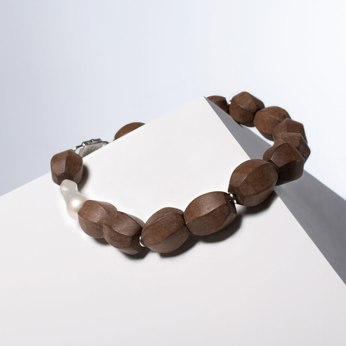 Light Walden faceted light brown wood beads and baroque pearl with silver-tone spacers, draped over a white block