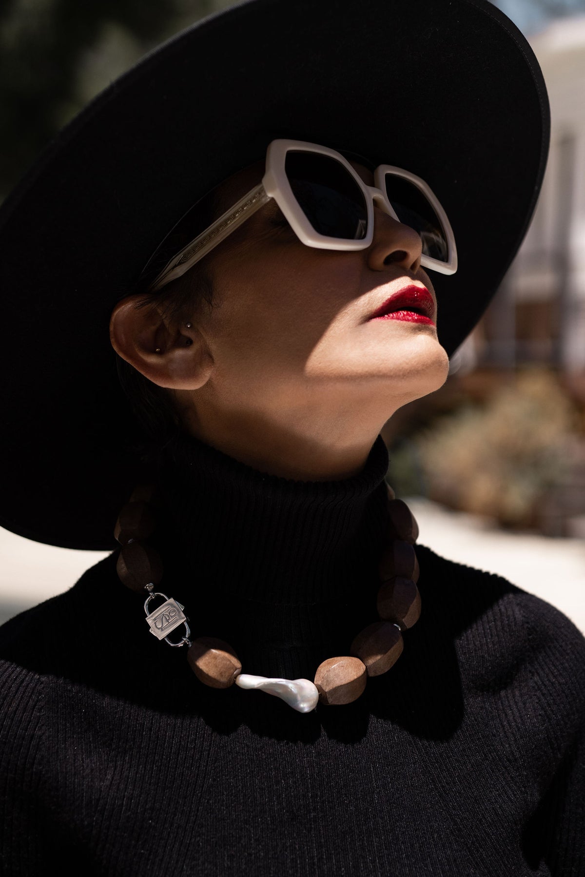 Profile of model in black hat and sunglasses, Light Walden wood and pearl necklace with HoS Lock