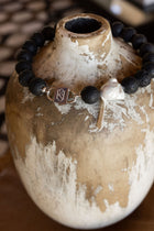 Luna lava stone necklace with baroque pearl and HoS Lock draped over a weathered vase