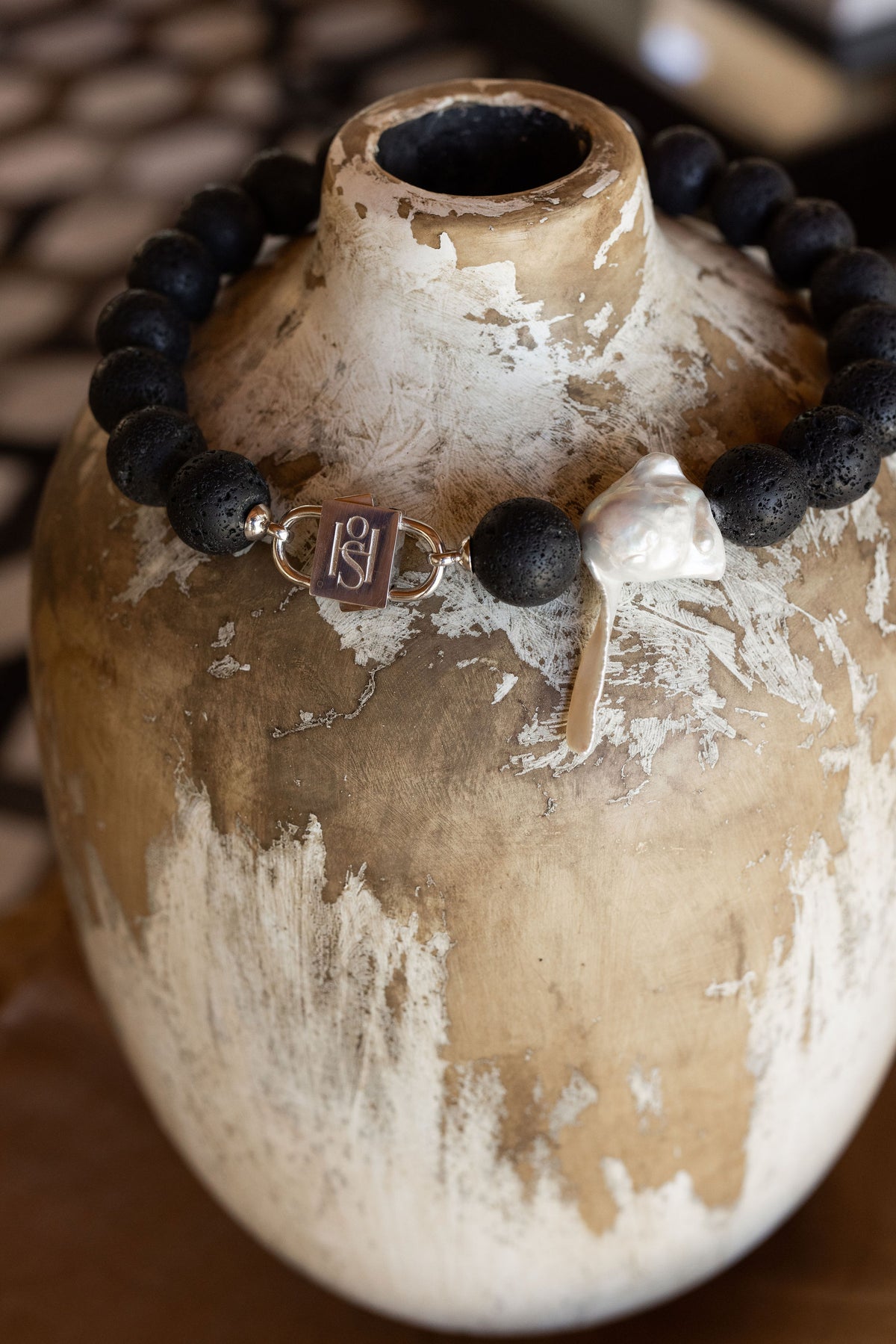 Luna lava stone necklace with baroque pearl and HoS Lock draped over a weathered vase