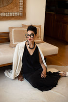 Model seated on the floor in a white coat and black dress wearing the Luna lava stone necklace
