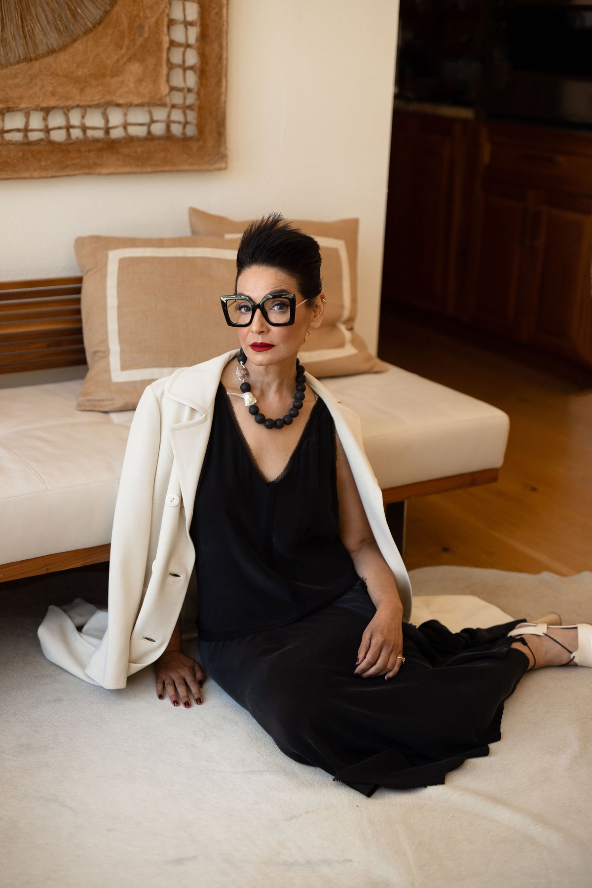 Model seated on the floor in a white coat and black dress wearing the Luna lava stone necklace