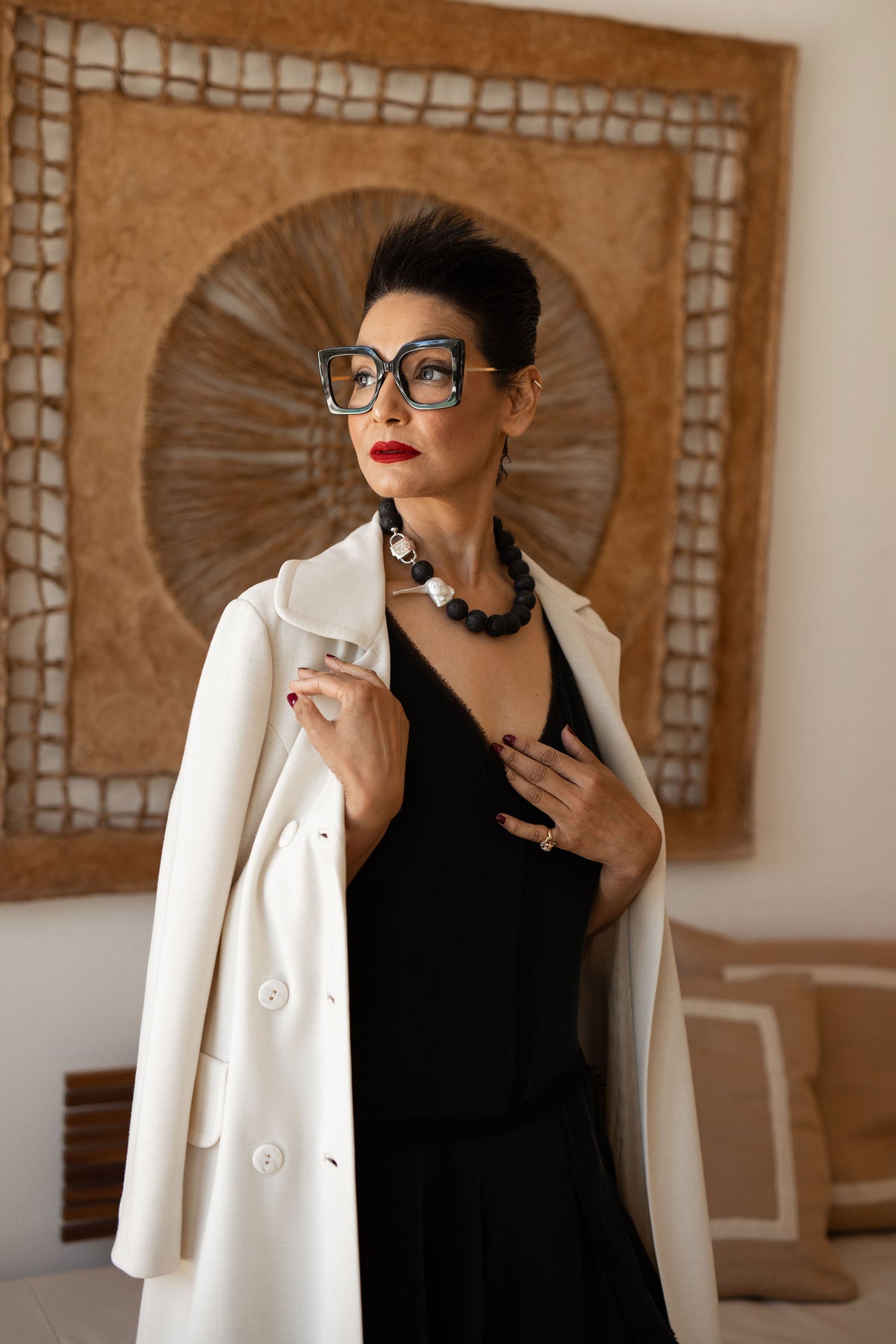 Model standing by woven wall art wearing the Luna lava stone necklace with baroque pearl