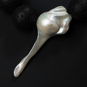 Close-up of the large fireball baroque pearl on the Luna necklace beside black lava stones