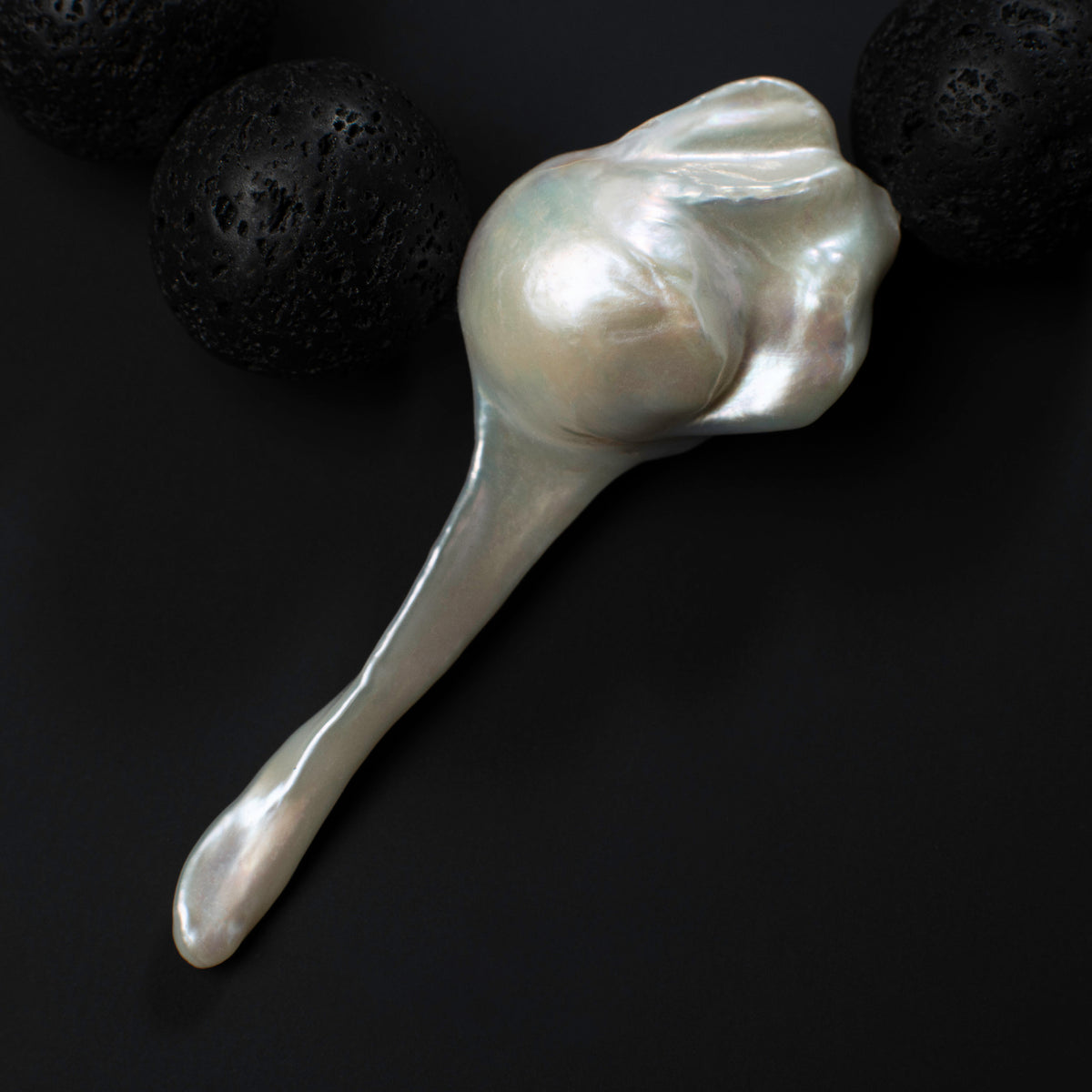 Close-up of the large fireball baroque pearl on the Luna necklace beside black lava stones